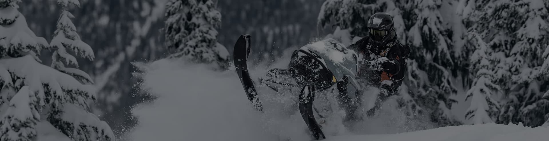 Снегоход Ski-Doo поднимает снежный шлейф на склоне в лесу
